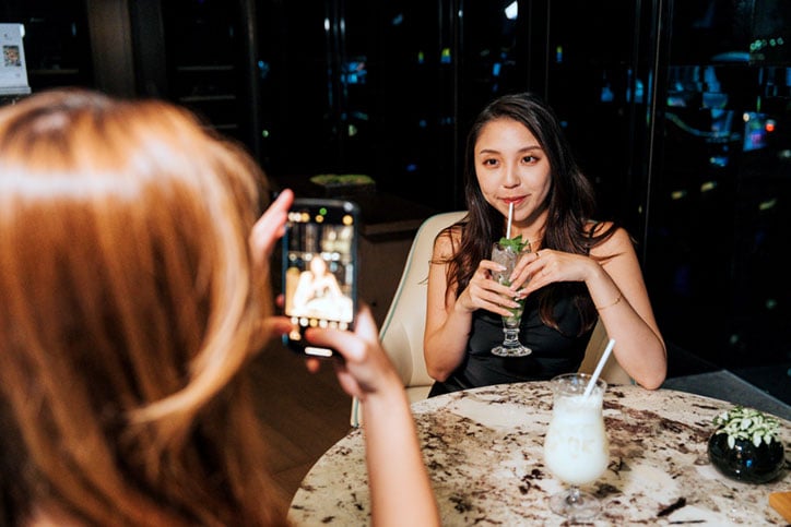 Happy Gen Z girls enjoying snacks and drinks at a bar in a hotel, taking some photos
