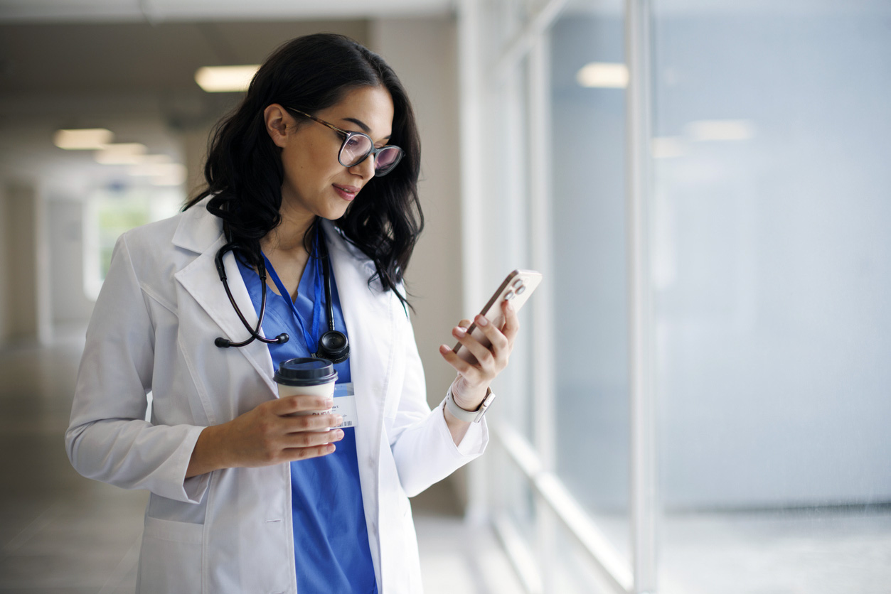 Smiling doctor with coffee cup and smartphone in modern hospital